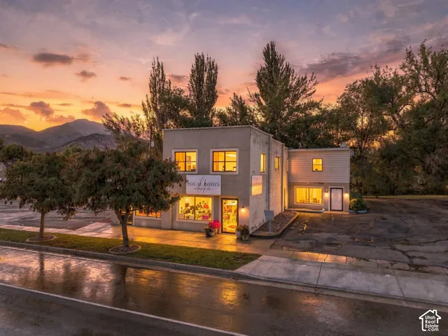Multi-level building exterior featuring stucco and horizontal siding, large storefront windows, paved parking area, and mountain backdrop