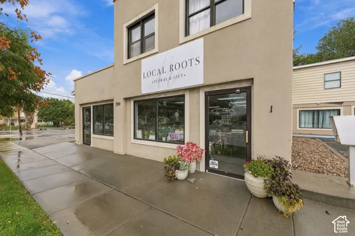 Stucco exterior featuring large storefront display windows, multiple glass-paneled entry doors, and a concrete sidewalk entrance