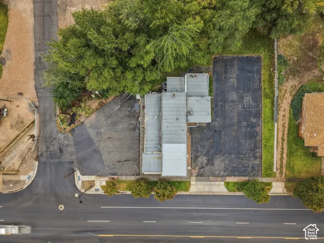 Aerial perspective of corner lot featuring multi-section asphalt paving, mature perimeter trees, and concrete sidewalk frontage