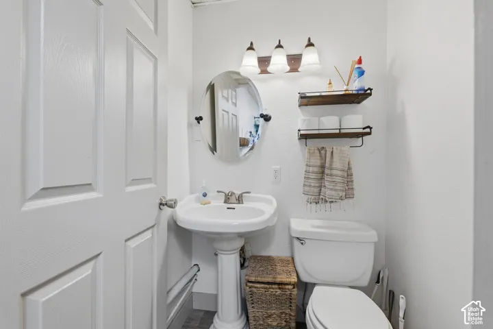 White pedestal sink with a dual-handle faucet, oval wall-mounted mirror, three-light vanity fixture with frosted glass shades, and wall-mounted shelving