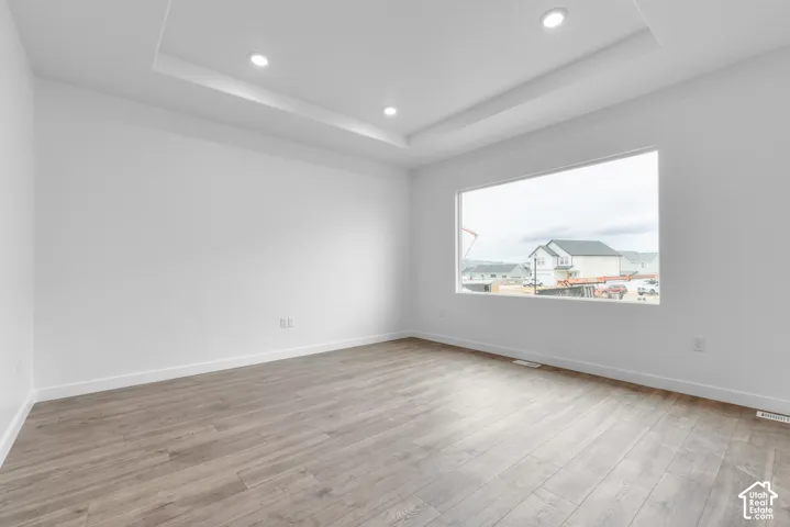 Tray ceiling with recessed lighting, large picture window, and wood-finish flooring