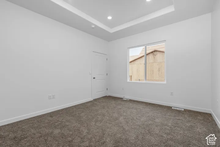 Neutral-toned interior room featuring a tray ceiling with recessed lighting, carpeted flooring, and a single-panel interior door