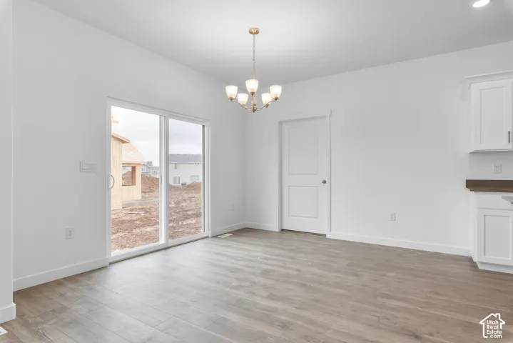 Interior space featuring wood-finish flooring, a multi-light chandelier, a sliding glass door, and white cabinetry with a wood-tone countertop