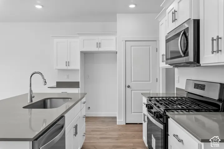 Kitchen featuring white shaker-style cabinetry, solid-surface countertops, stainless steel appliances, an island with an undermount sink, and wood-finish flooring