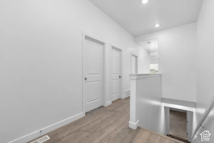Neutral interior hallway featuring wood-finish flooring, white walls, paneled doors with metallic hardware, and recessed lighting