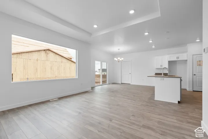 Open-concept living space featuring wood-finish flooring, recessed lighting, a tray ceiling, an expansive picture window, and a kitchen island with a built-in sink