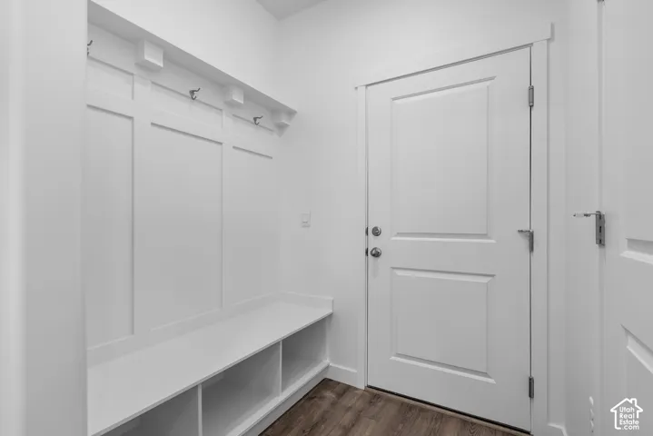 Built-in storage bench featuring partitioned cubbies, white wall paneling, integrated metal hooks, and wood-finish flooring