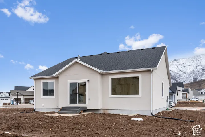 Exterior facade featuring light-toned stucco siding, a gabled roofline, sliding glass rear entry, and mountain backdrop