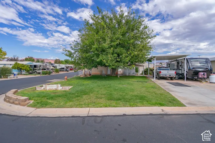 Corner lot featuring a manicured lawn, mature shade tree, concrete driveway, and a covered carport