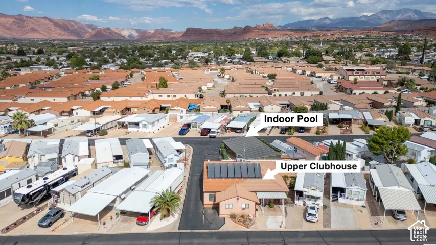Aerial perspective featuring the community clubhouse with rooftop solar panels, indoor pool facilities, and surrounding desert mountain range