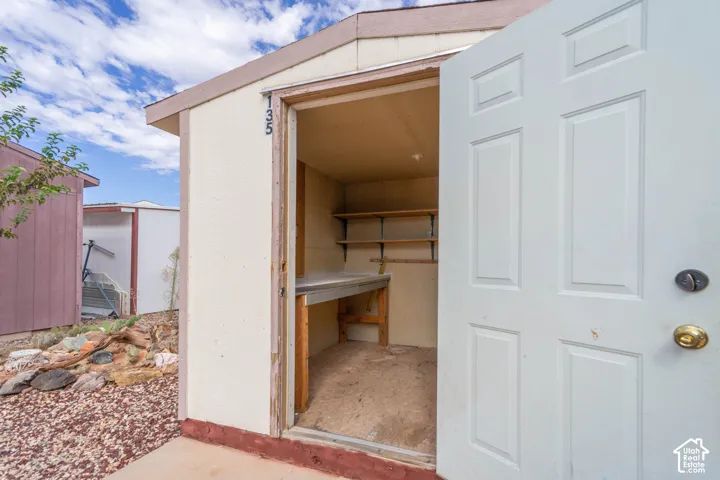 Exterior storage structure featuring a paneled door, interior built-in wooden shelving, and a solid work surface