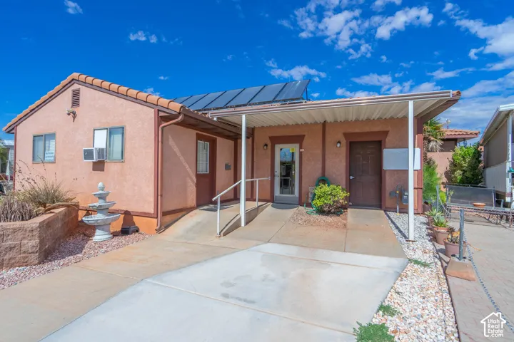 Stucco exterior featuring a concrete entry ramp, a covered porch with metal awning, and rooftop solar panels