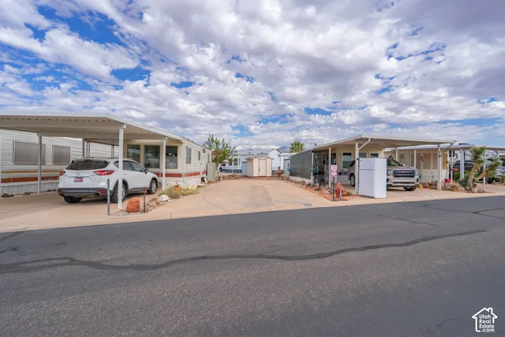 Concrete parking area featuring two covered carports, detached storage shed, and exterior desert landscaping