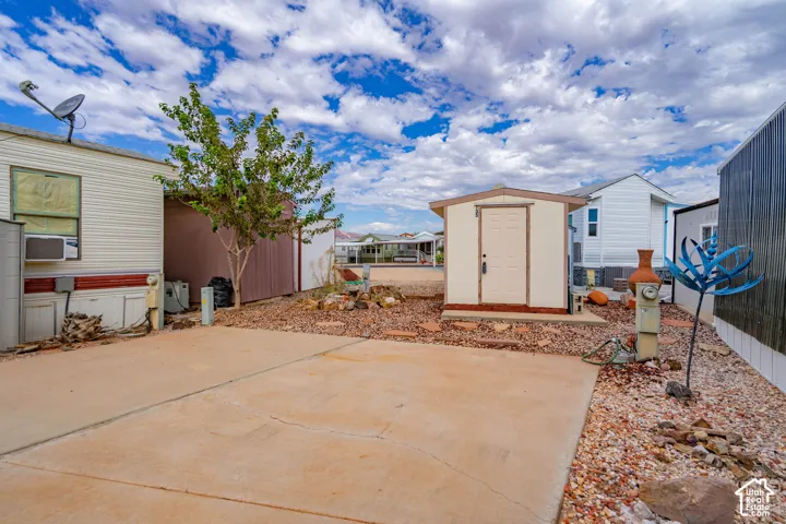 Concrete parking pad featuring a detached storage shed, gravel landscaping, and mature tree