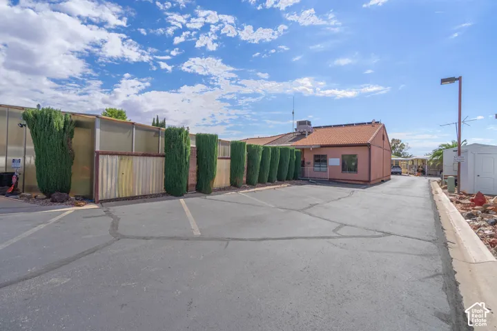 Exterior view featuring an asphalt parking lot, privacy fencing, manicured evergreen landscaping, and a low-pitch roof structure