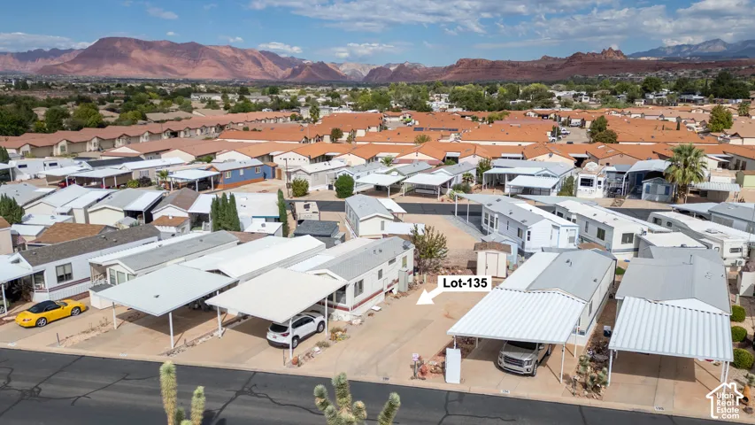Aerial perspective of lot-135 featuring an open parking space, a metal carport, and a detached storage structure, set against a backdrop of prominent red rock formations