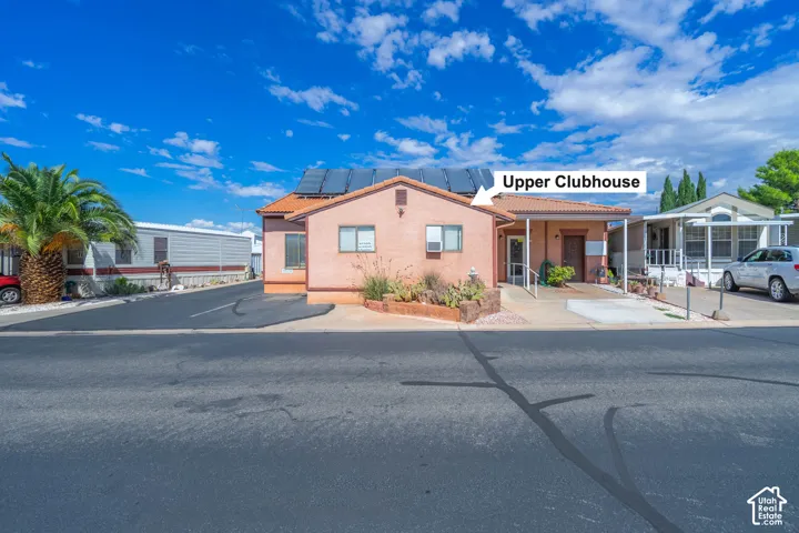 Clubhouse facility featuring a stucco exterior, tile roofing, roof-mounted solar panels, and a paved parking surface