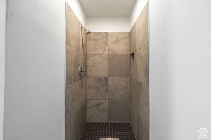 Walk-in shower featuring large-format neutral stone-style wall tile, dark mosaic floor tile, built-in recessed wall niche, and polished chrome shower fixture