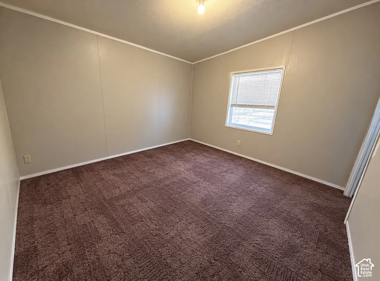 Neutral-toned wall panels, wall-to-wall carpeting, and a single-pane window with horizontal blinds