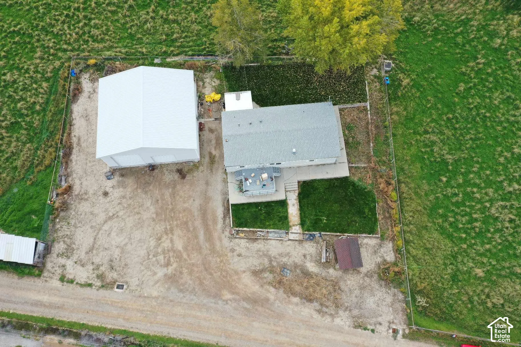 Aerial perspective of property featuring a detached metal garage, fenced perimeter, grass lawn, concrete patio, and gravel driveway