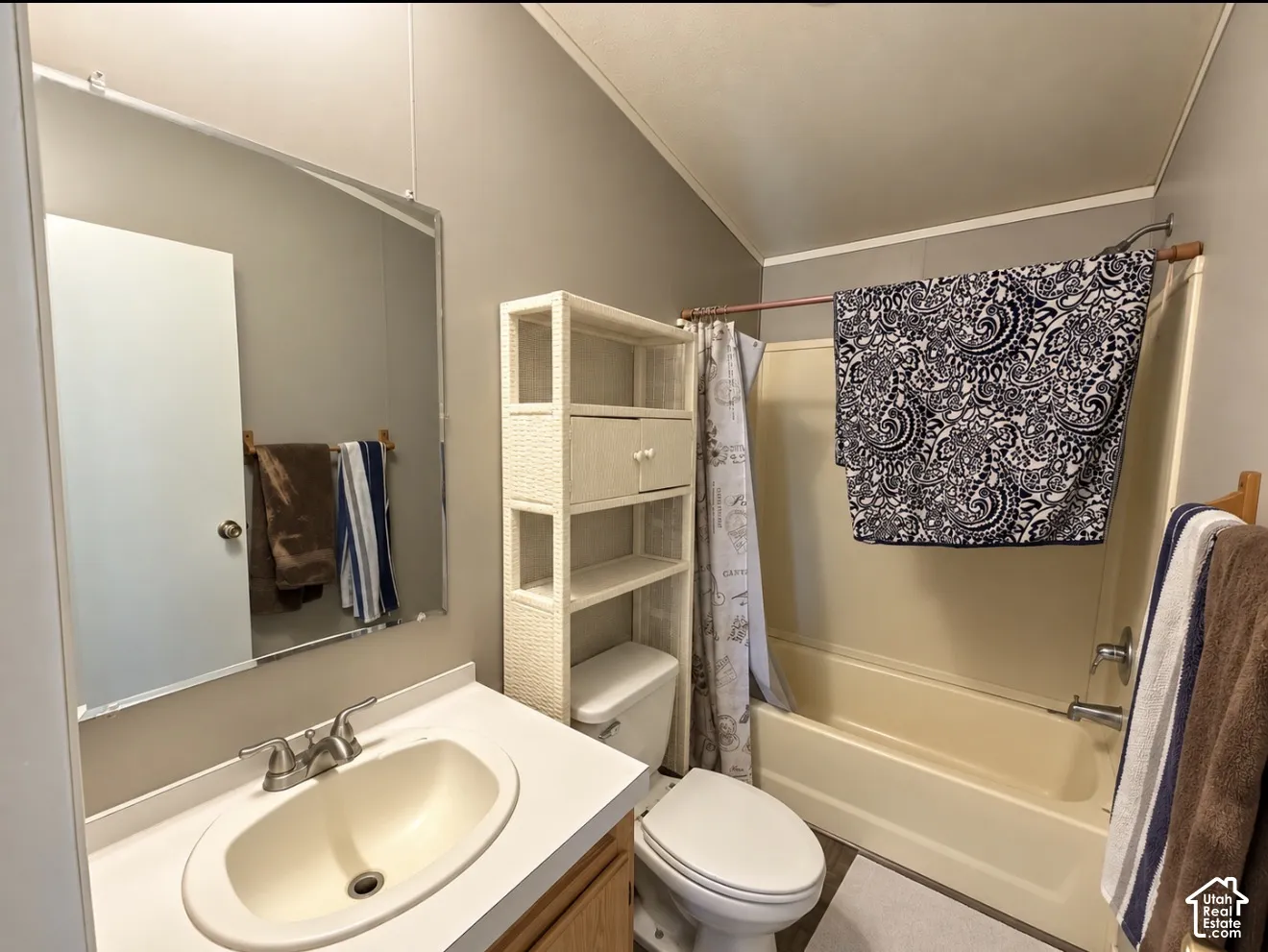 Bathroom featuring an integrated vanity with a molded basin, a wall-mounted mirror, a tub-shower combination with a surround, and a vaulted ceiling