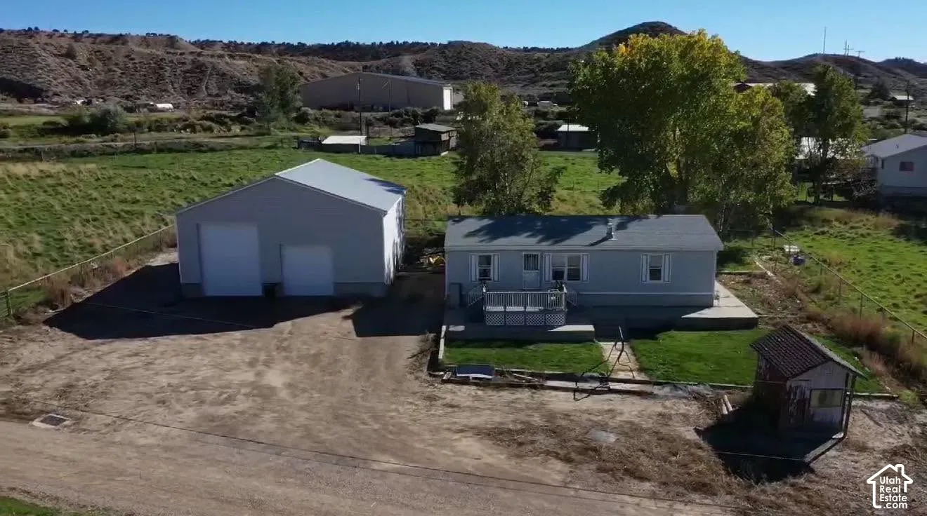 Single-level exterior featuring a metal-sided detached garage, a concrete patio, an elevated wooden deck, and a fenced lot with mountain scenery