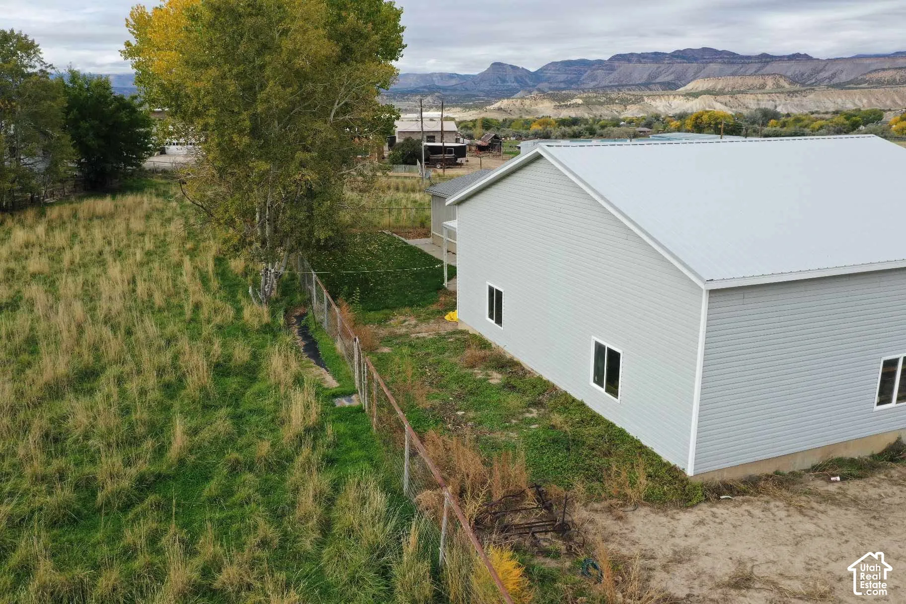 Exterior featuring light-colored horizontal siding, a metal roof, and a fenced perimeter with prominent mountain scenery