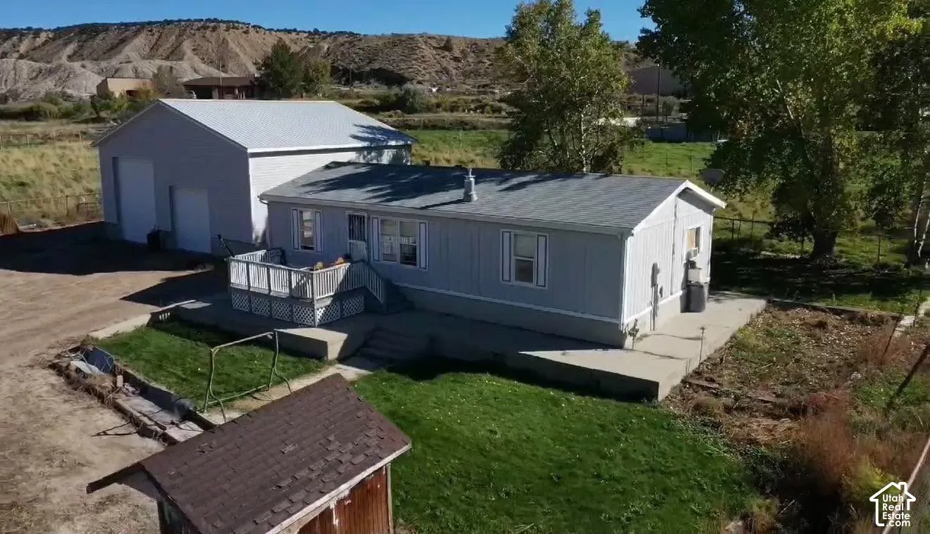Single-story residence featuring light gray siding, a composite shingle roof, a detached garage, a raised deck with railing, and a concrete patio