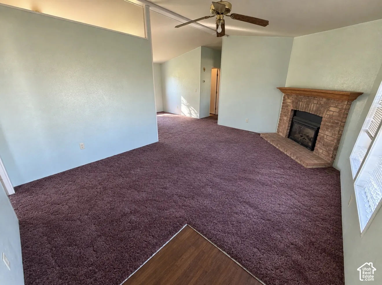 Interior space featuring vaulted ceilings, a masonry fireplace with a wood mantel, a ceiling fan, and carpeted flooring