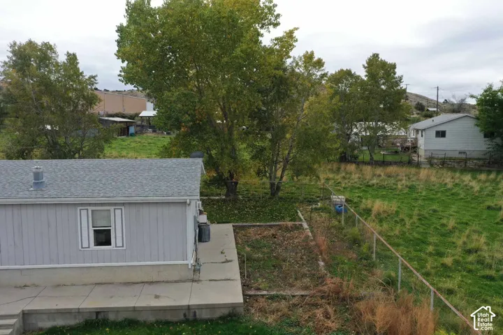 Exterior featuring light-gray horizontal siding, a concrete patio, a metal chain-link fence, and mature trees on the grounds