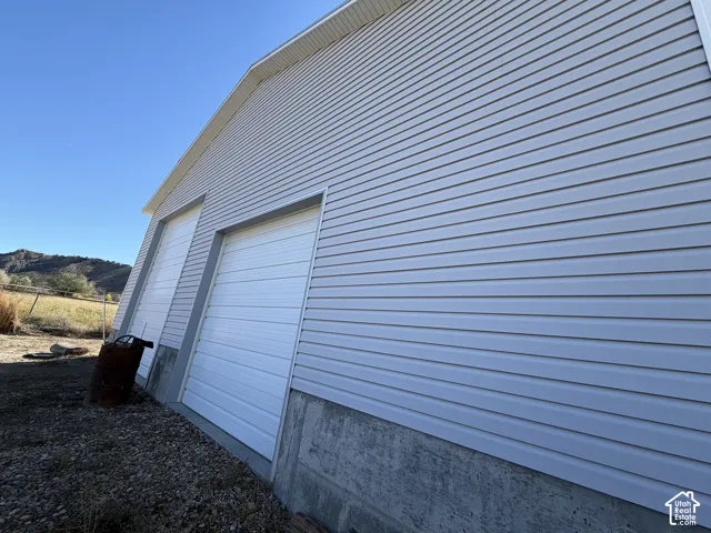 Exterior featuring light-colored horizontal siding, two white roll-up garage doors, a concrete foundation, and a mountain backdrop