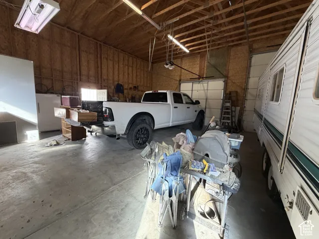 Oversized detached garage featuring high ceilings, exposed wood-frame construction, concrete flooring, and multiple overhead garage doors