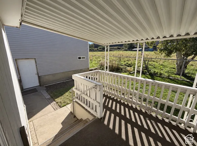 Covered porch featuring a metal canopy, white railing, and metal support posts with decorative accents, providing access to a concrete pathway and exterior entryway