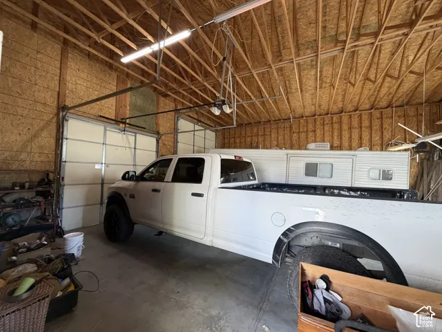 Spacious garage featuring exposed wood-truss ceiling, high-clearance overhead doors, and concrete flooring