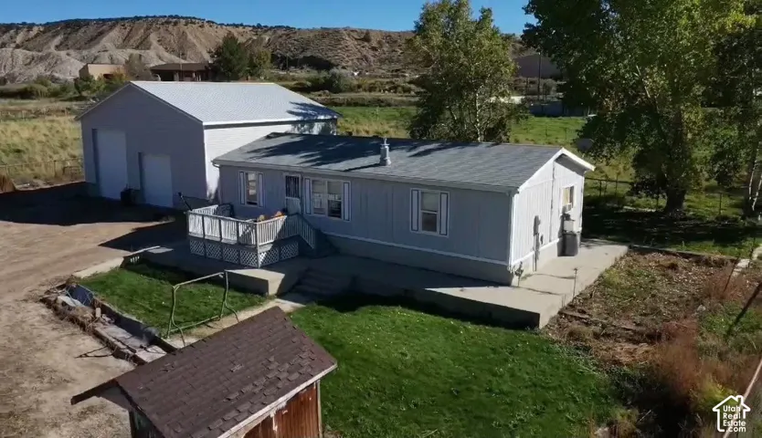 Single-story residence featuring light gray siding, a composite shingle roof, a detached garage, a raised deck with railing, and a concrete patio