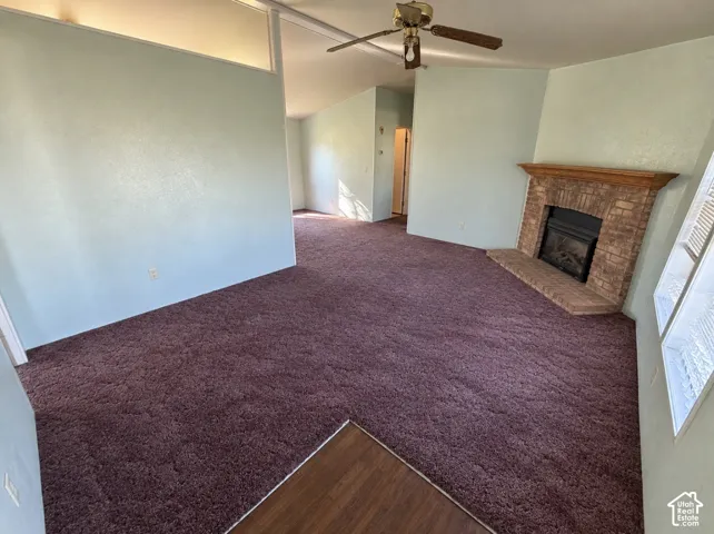 Interior space featuring vaulted ceilings, a masonry fireplace with a wood mantel, a ceiling fan, and carpeted flooring