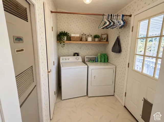 Utility room featuring a natural wood-finish wall-mounted shelf, a built-in metal utility closet, patterned wall covering, sheet vinyl flooring, and an exterior door with integrated glass panels