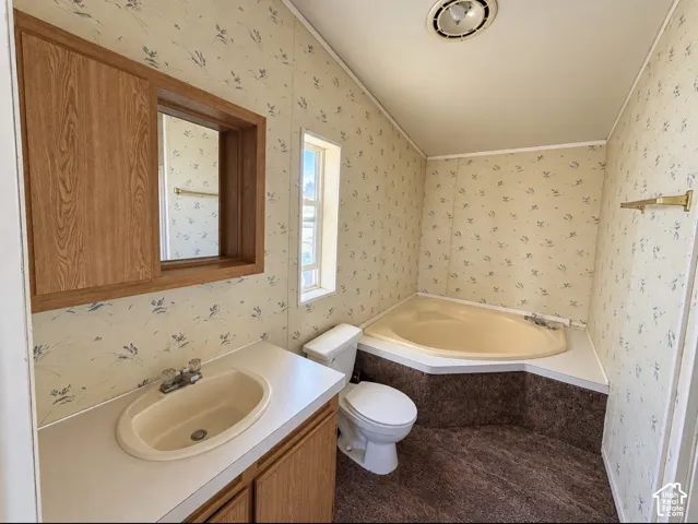 Built-in wood-finish vanity with an integrated sink, corner garden tub with a textured surround, recessed ceiling lighting, and a wall-mounted medicine cabinet