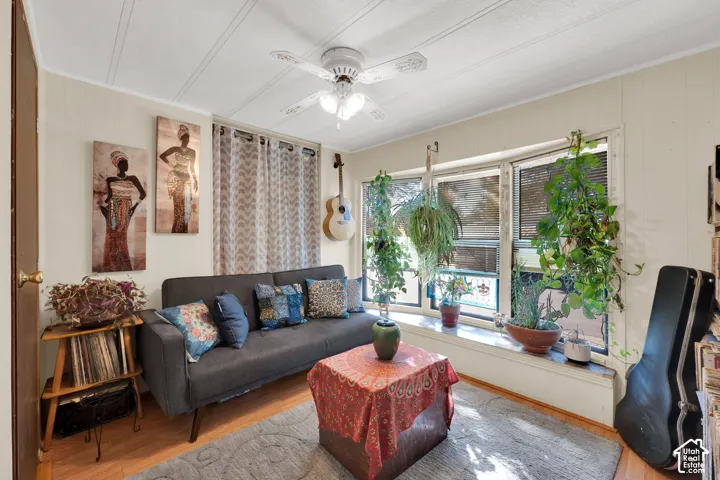 Interior room featuring wood-finish flooring, a multi-pane bay window with a wide sill, aa white ceiling fan with lighting