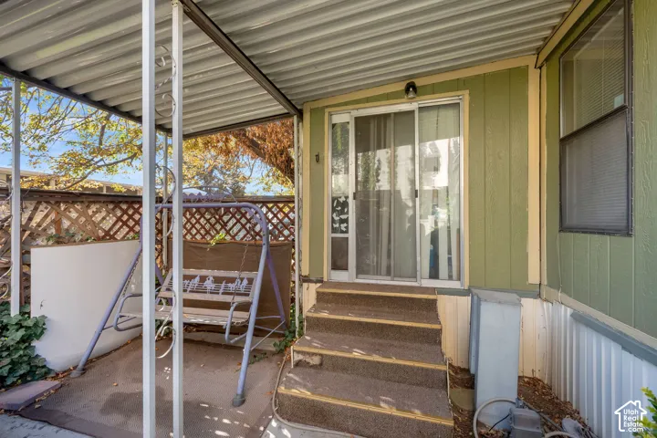Covered patio area featuring vertical siding, sliding glass door entry, concrete flooring, and latticework fencing