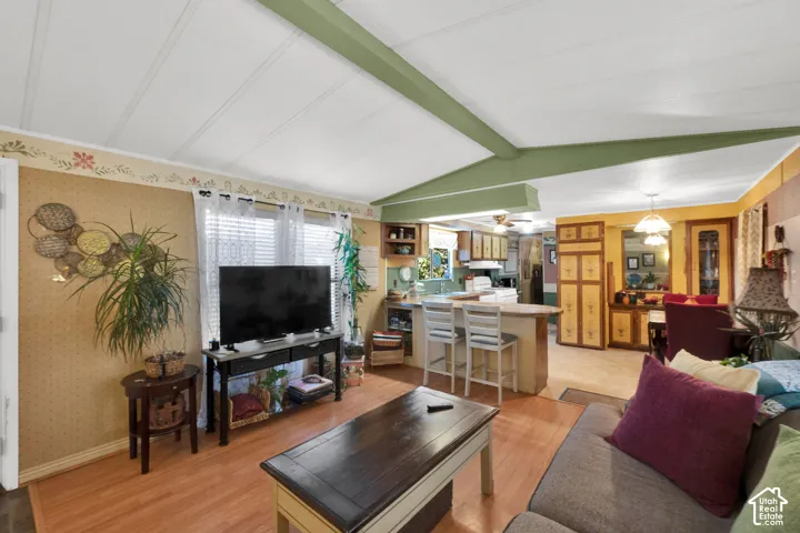 Vaulted ceiling with exposed decorative beam, wood-finish flooring, and kitchen featuring a peninsula breakfast bar and built-in cabinetry