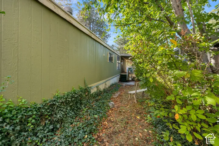 Exterior side elevation featuring vertical panel siding, mature vegetation, and a covered entry