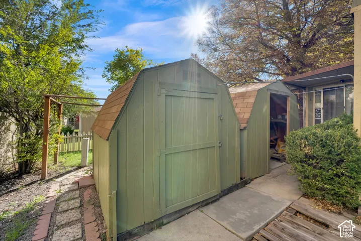 Dual outdoor storage structures featuring gable rooflines, wood siding, and asphalt shingles, complemented by a concrete walkway
