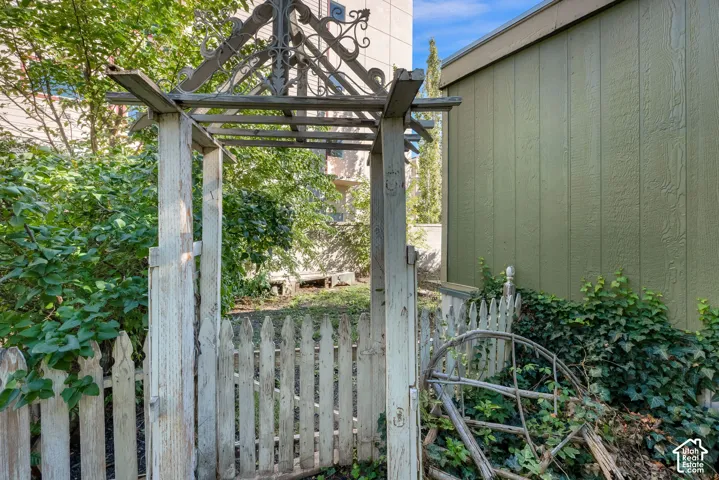 Custom wood garden arbor with decorative metal fretwork, complemented by a white picket fence and vertical-panel exterior siding