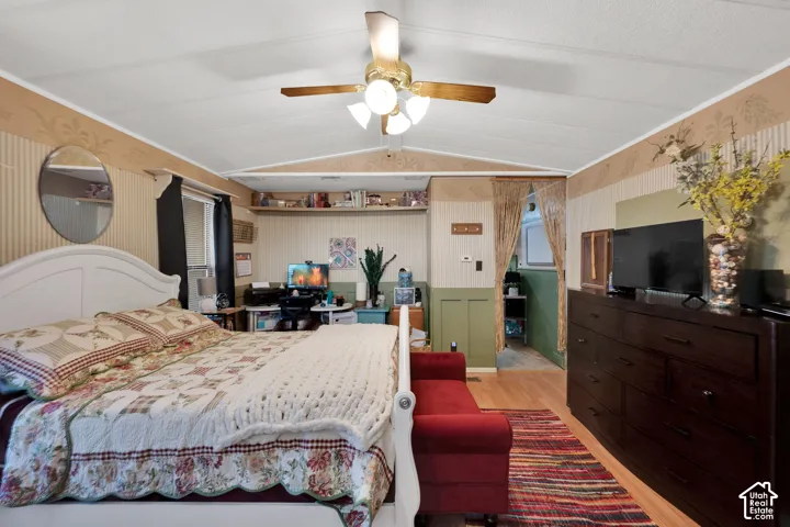 Vaulted ceiling featuring a central multi-light fan, wood-finish flooring, built-in shelving, and wainscoting