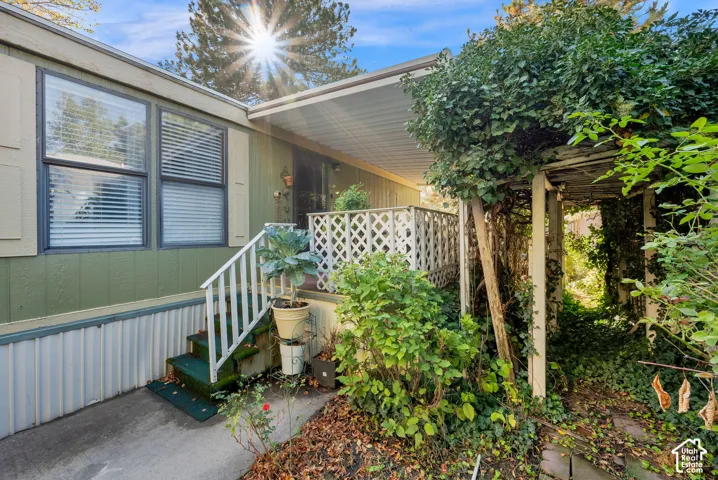 Exterior featuring a covered porch with white lattice railing, concrete entryway, and a vine-covered pergola