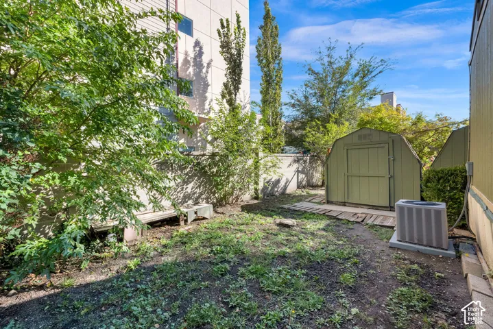 Private outdoor space featuring perimeter concrete wall fencing, a detached storage shed, mature trees, and an external HVAC unit