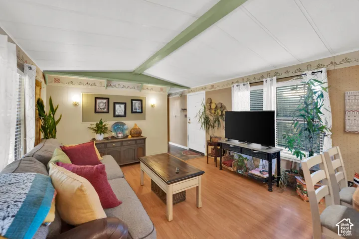 Living space featuring vaulted ceilings, a central structural beam, wood-finish flooring, wall-mounted light fixtures, and windows with integrated blinds