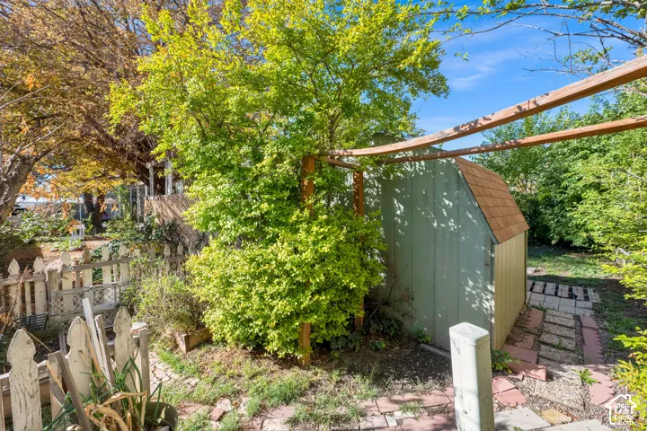 Exterior storage shed with a shingled roof, timber pergola, and decorative picket fencing