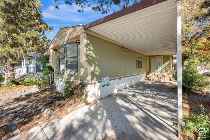 Exterior featuring vertical siding, metal carport, concrete driveway, and stairs leading to the entry